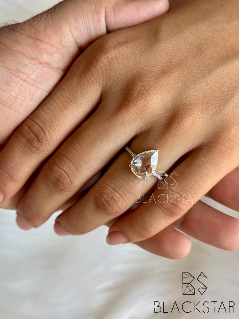 On-hand view of a luxurious pear shaped lab grown diamond engagement ring worn on finger, showcasing a brilliant pear cut center diamond with a delicate halo and pavé diamond band. Crafted in polished white gold, this elegant ring highlights exceptional sparkle, balanced proportions, and refined craftsmanship. Ideal for buyers searching pear diamond engagement rings, lab created diamond jewelry, ethical bridal rings, modern luxury engagement rings, and sustainable fine jewelry.