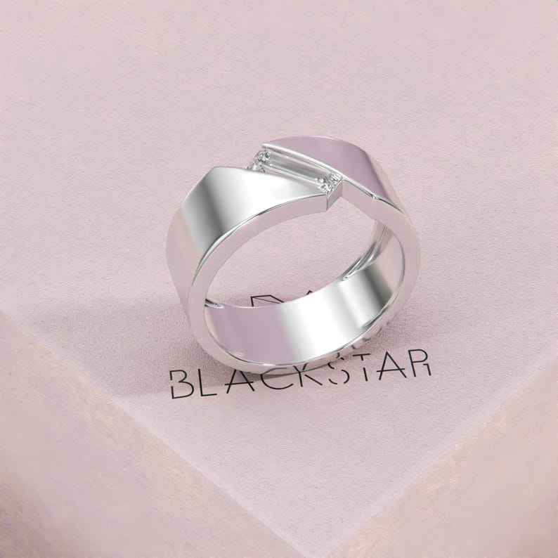 K&ouml;nnte beinhalten: Ein silberner Ring mit modernem Design. Der Ring hat eine geometrische Form mit einem kleinen, klaren Steinakzent. Das Wort "BLACKSTAR" ist im Hintergrund zu sehen. Der Ring wird auf einer rosa Oberfl&auml;che pr&auml;sentiert.