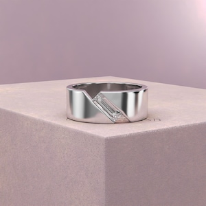 K&ouml;nnte beinhalten: Ein silberner Ring mit geometrischem Design. Der Ring hat einen rechteckigen, klaren Edelstein, der diagonal &uuml;ber einen Teil des Bandes gesetzt ist. Das Band hat einen modernen, minimalistischen Stil mit poliertem Finish.