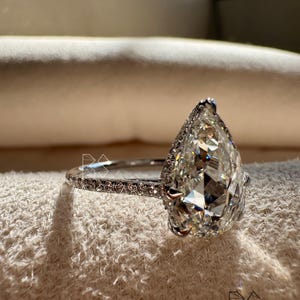 Side profile close-up of a pear shaped lab grown diamond engagement ring featuring a sparkling halo and pavé accented white gold band. The elongated pear diamond is expertly set to maximize light performance and elegance. Designed for modern brides, this ring combines luxury with sustainability, making it ideal for searches such as pear lab diamond engagement ring, ethical diamond jewelry, luxury bridal ring, and contemporary fine jewelry designs.