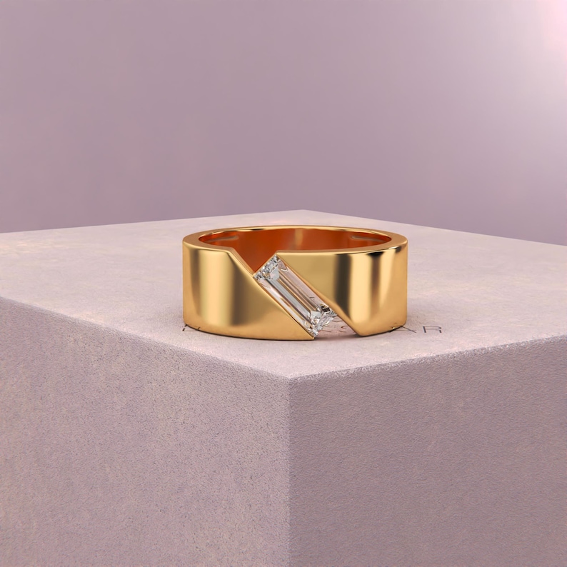K&ouml;nnte beinhalten: Ein goldener Ring mit einem einzigartigen Design. Der Ring verf&uuml;gt &uuml;ber einen rechteckigen, klaren Edelstein, der diagonal &uuml;ber einen Teil des Bandes gesetzt ist. Das Band selbst ist aus dickem, poliertem Gold, was einen modernen und eleganten Look erzeugt. Der Ring wird auf einer neutralen Oberfl&auml;che pr&auml;sentiert.