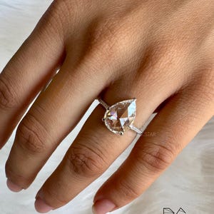 Angled on-hand close-up of a pear cut lab grown diamond engagement ring featuring a luminous pear shaped center stone framed by a fine diamond halo and pavé set white gold band. The ring’s elegant silhouette enhances brilliance and finger coverage, making it perfect for modern brides. Designed for those seeking lab grown pear diamond rings, ethical engagement jewelry, luxury bridal rings, handmade diamond rings, and contemporary fine jewelry designs.