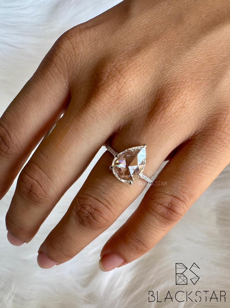 Angled on-hand close-up of a pear cut lab grown diamond engagement ring featuring a luminous pear shaped center stone framed by a fine diamond halo and pavé set white gold band. The ring’s elegant silhouette enhances brilliance and finger coverage, making it perfect for modern brides. Designed for those seeking lab grown pear diamond rings, ethical engagement jewelry, luxury bridal rings, handmade diamond rings, and contemporary fine jewelry designs.