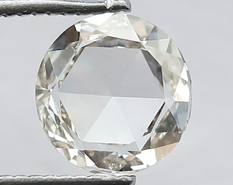 Könnte beinhalten: Ein runder, facettierter Diamant, der von einer silbernen Pinzette gehalten wird. Der Diamant ist klar mit mehreren Facetten, die das Licht reflektieren. Der Edelstein ist farbneutral und erscheint fast farblos.