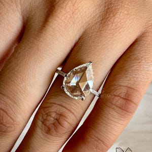 Side profile close-up of a pear cut lab grown diamond engagement ring showcasing the elevated setting, halo diamonds, and pavé accented white gold band. The refined prong work enhances light performance while maintaining a sleek, modern profile. Perfect for buyers searching pear shaped diamond engagement rings, lab grown diamonds, ethical bridal jewelry, luxury handmade rings, and contemporary engagement ring styles.