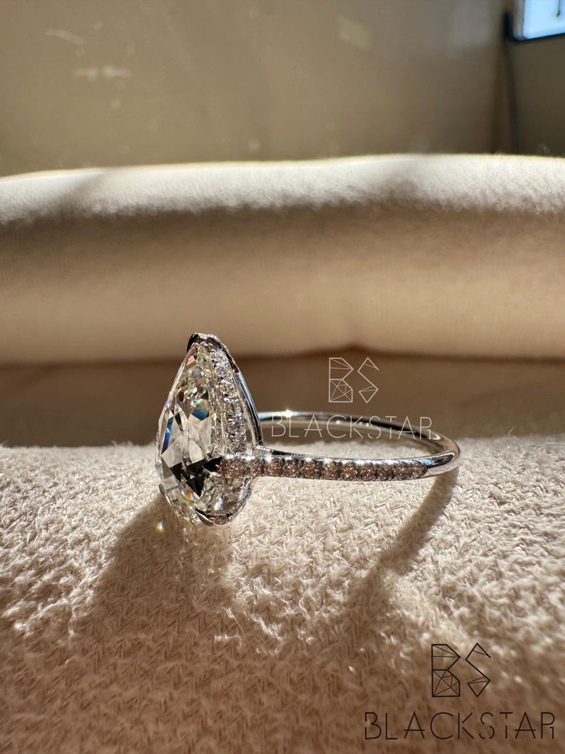 Side angle view of a pear cut lab grown diamond ring emphasizing the pavé diamond band and refined prong work around the halo setting. The white gold band offers a sleek, elegant finish while enhancing durability and comfort. This sophisticated engagement ring suits customers looking for pear shaped diamond rings, lab grown diamonds, ethical engagement rings, sustainable fine jewelry, and premium handcrafted bridal jewelry.