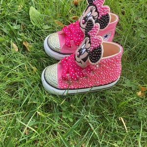 Puede incluir: Un par de zapatillas altas rosas con suelas blancas y puntera dorada. Las zapatillas est&aacute;n adornadas con cuentas rosas y presentan una aplicaci&oacute;n de Minnie Mouse en la leng&uuml;eta. Los cordones son rosas con lunares blancos.