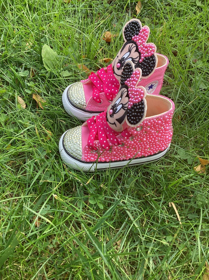 Puede incluir: Un par de zapatillas altas rosas con suelas blancas y puntera dorada. Las zapatillas est&aacute;n adornadas con cuentas rosas y presentan una aplicaci&oacute;n de Minnie Mouse en la leng&uuml;eta. Los cordones son rosas con lunares blancos.