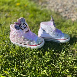 May include: A pair of custom-designed high-top sneakers, one featuring a Minnie Mouse design with pink and purple embellishments, the other with a star design. Both shoes have white uppers, red soles, and are decorated with rhinestones and pearls.