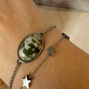 May include: A silver chain bracelet with a green and white oval stone pendant and silver star charms.