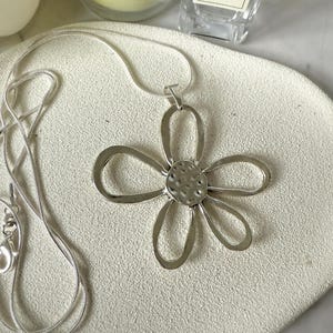 May include: A silver chain necklace with a silver flower pendant. The flower has a textured center and five petals.