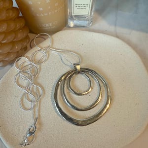 Op de afbeelding: Een zilveren ketting met een hanger met drie concentrische cirkels. De cirkels zijn gehamerd en hebben een textuur.