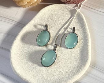 May include: A jewellery set comprising a necklace and matching earrings. Each piece has a silver-toned metal setting with an oval, light blue gemstone. The set is displayed on a white, textured surface.