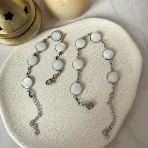 May include: Two silver bracelets with white round shell-like charms. The bracelets have a lobster clasp closure.