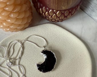 May include: A silver chain necklace with a black crescent moon pendant. The pendant has a textured, almost rough surface.