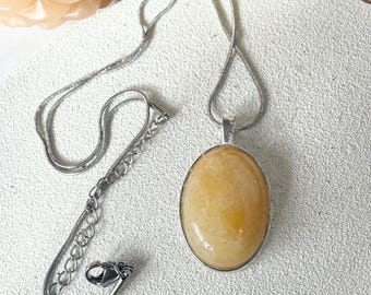 May include: A silver chain necklace with a light yellow oval pendant. The pendant is made of a smooth, translucent stone.