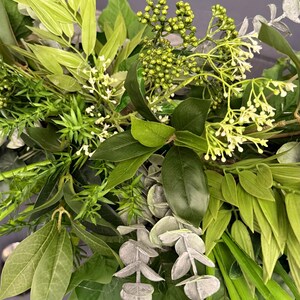 May include: A close-up of a variety of green foliage, including eucalyptus, ferns, and other leafy plants. The foliage is arranged in a lush and natural way, creating a beautiful and vibrant display.