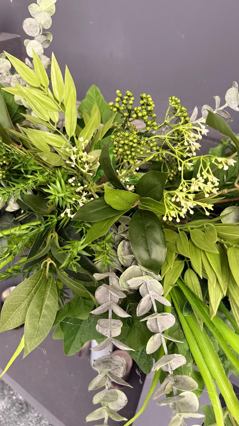 May include: A close-up of a variety of green foliage, including eucalyptus, ferns, and other leafy plants. The foliage is arranged in a lush and natural way, creating a beautiful and vibrant display.