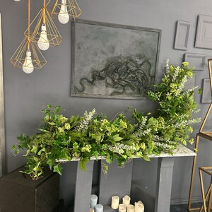 Pode incluir: Uma lareira cinza com uma guirlanda verde de folhas e flores. A lareira &eacute; decorada com velas azuis e brancas.