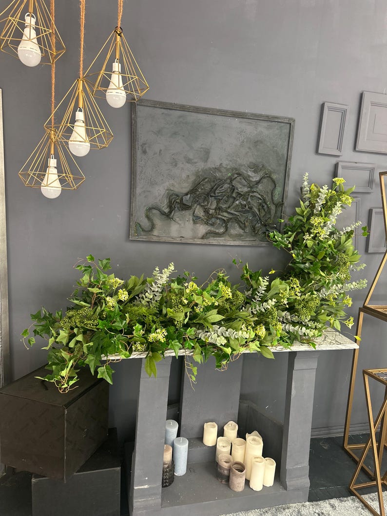 Pode incluir: Uma lareira cinza com uma guirlanda verde de folhas e flores. A lareira &eacute; decorada com velas azuis e brancas.