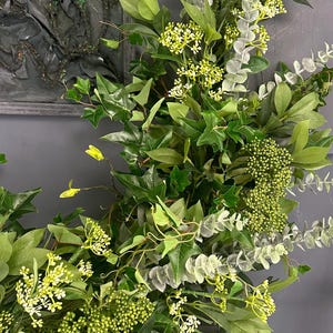 Pode incluir: Uma guirlanda verde exuberante com eucalipto, hera e pequenas flores brancas. A guirlanda &eacute; perfeita para adicionar um toque de natureza a qualquer espa&ccedil;o.