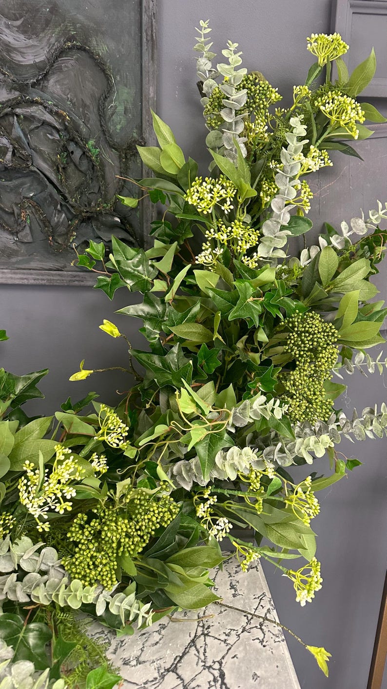 Pode incluir: Uma guirlanda verde exuberante com eucalipto, hera e pequenas flores brancas. A guirlanda &eacute; perfeita para adicionar um toque de natureza a qualquer espa&ccedil;o.