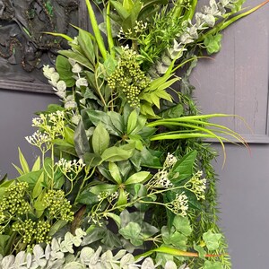 May include: A lush green and silver artificial plant arrangement with a variety of leaves and flowers. The arrangement is perfect for adding a touch of nature to any room.