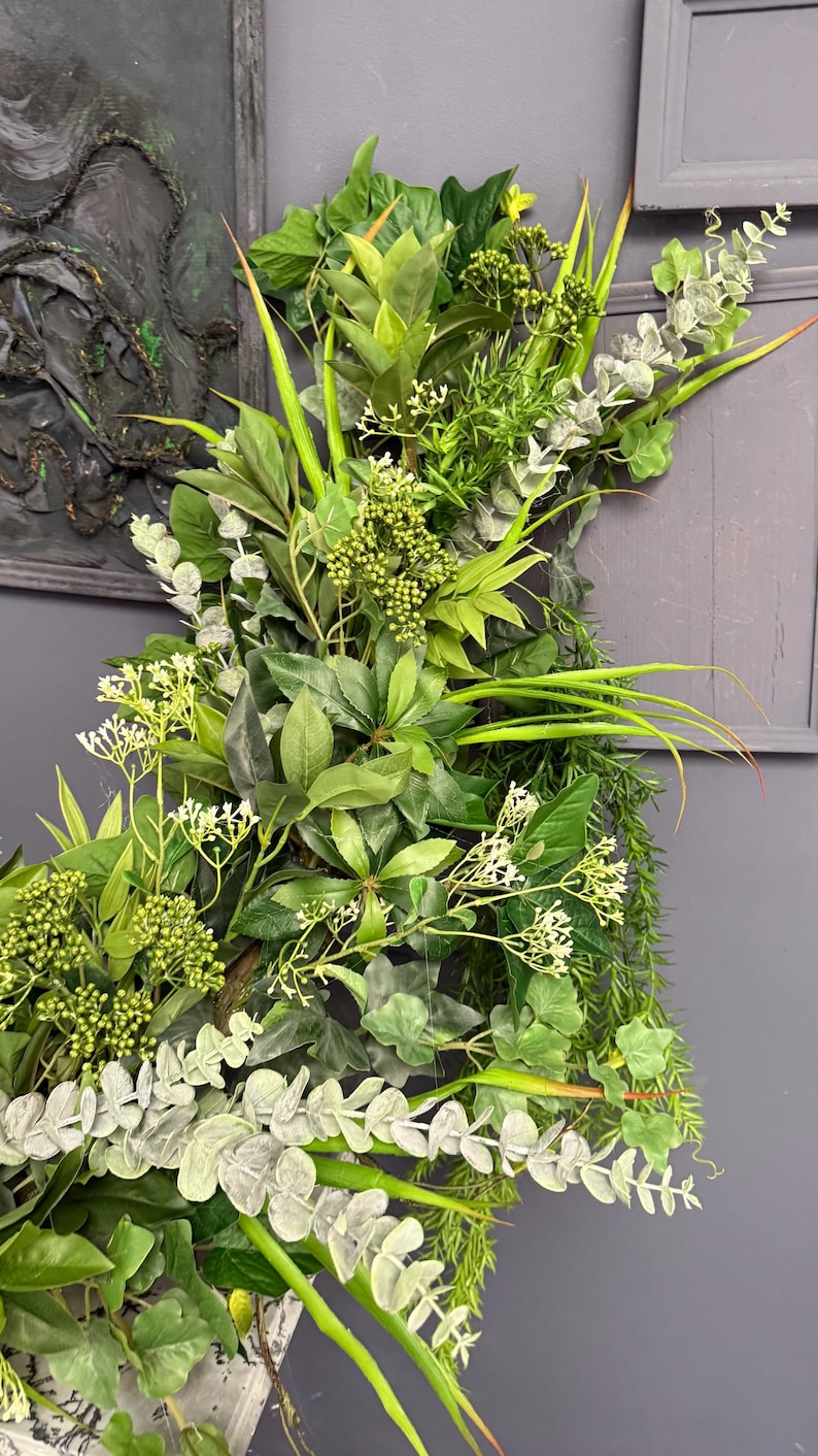 May include: A lush green and silver artificial plant arrangement with a variety of leaves and flowers. The arrangement is perfect for adding a touch of nature to any room.