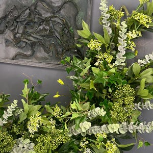 Pode incluir: Uma guirlanda verde exuberante feita de eucalipto, hera e outras plantas verdes. A guirlanda est&aacute; drapeada sobre uma lareira de m&aacute;rmore branco.