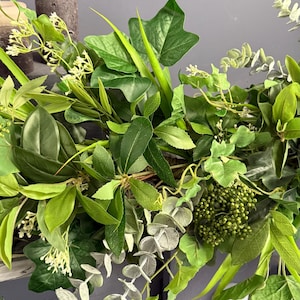 May include: A lush green garland with eucalyptus, ivy, and other greenery. The garland is draped over a mantle and is decorated with small white flowers.