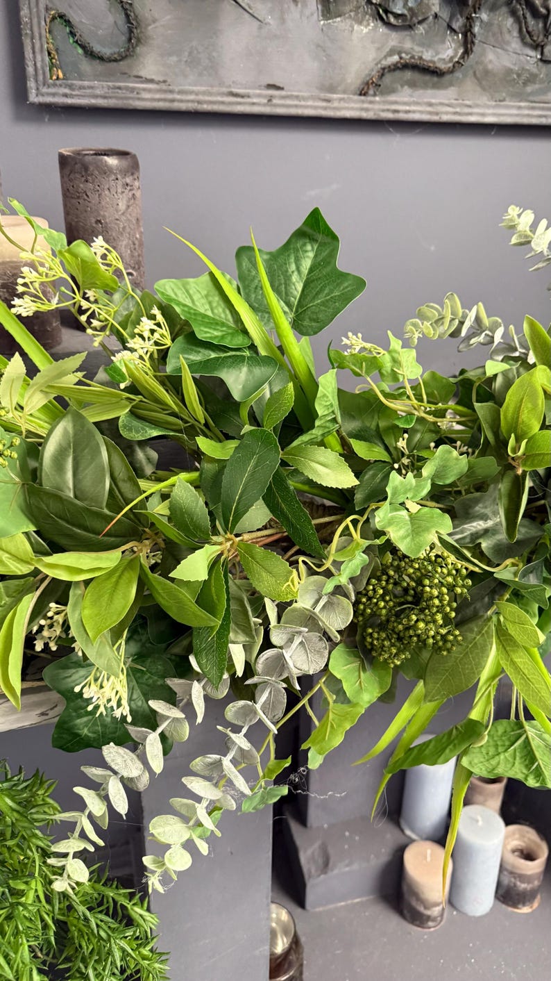 May include: A lush green garland with eucalyptus, ivy, and other greenery. The garland is draped over a mantle and is decorated with small white flowers.