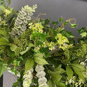 Pode incluir: Uma guirlanda verde com eucalipto, hera e pequenas flores brancas. A guirlanda est&aacute; drapeada sobre uma prateleira com velas.