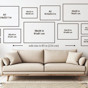 May include: A beige sofa measuring 85 inches in width positioned below a wall display of eleven empty black rectangular frames. Each frame features printed text indicating various dimensions in inches and centimeters, such as A1, 36x24, and 5x7.