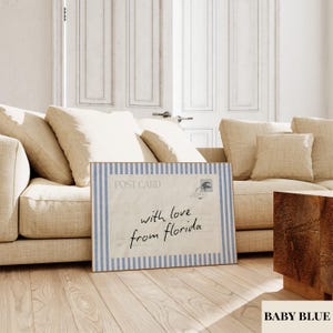 May include: A rectangular wall art print featuring a vintage postcard design with a light blue and white vertical striped border. The center displays the text "POST CARD" and the handwritten script "with love from florida" in black ink.