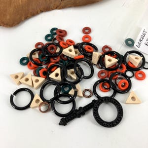 May include: A collection of bracelet-making supplies, including black, orange, red, green, and beige beads. The assortment includes round, triangular, and decorative elements. A small bag with the text "BRACELET KIT" is visible.