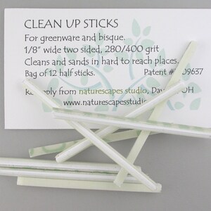 May include: A collection of white, rectangular Clean Up Sticks for greenware and bisque, with a card that reads "CLEAN UP STICKS". The sticks are 1/8" wide, two-sided, and 280/400 grit, designed for cleaning and sanding hard-to-reach places. The bag contains 12 half sticks.