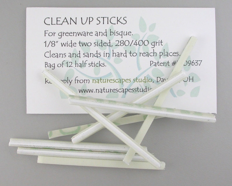 May include: A collection of white, rectangular Clean Up Sticks for greenware and bisque, with a card that reads "CLEAN UP STICKS". The sticks are 1/8" wide, two-sided, and 280/400 grit, designed for cleaning and sanding hard-to-reach places. The bag contains 12 half sticks.
