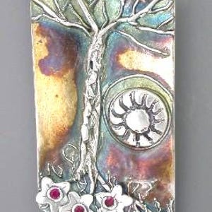 May include: A rectangular silver pendant with a tree design, a sunburst, and flowers with red centers. The pendant has a loop at the top for a chain. The metal has a colorful, iridescent finish.