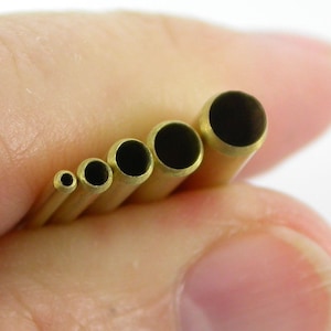 May include: A set of six brass tubes with different sized openings. The tubes are held in a hand, with the openings facing the camera.