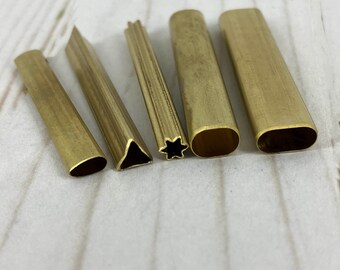 May include: Five brass metal tools with different shaped cutouts. The tools are arranged in a row from left to right. The cutouts are a rounded oval, a triangle, a star, a rounded oval, and a long oval.