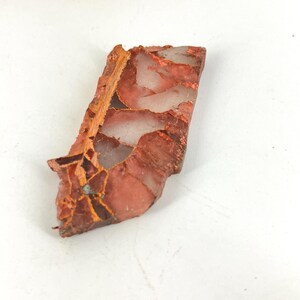 May include: A natural stone slab with a mix of red, brown, and white colors. The stone has a rough, textured surface and irregular shape. The stone appears to be a decorative item or a piece of art.