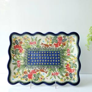 May include: A rectangular ceramic serving platter with a scalloped dark blue rim. The platter features a forest scene with foxes, red berries, and mushrooms. The center has a blue and yellow floral pattern.
