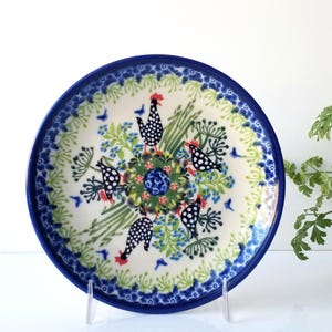May include: A blue and white ceramic plate with a floral design and a pattern of black and white chickens. The plate has a green and white border.