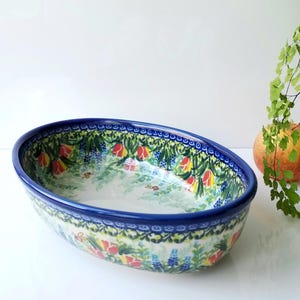 May include: Oval ceramic serving bowl with a blue rim and floral pattern. The bowl features a colorful design of red, yellow, and blue flowers with green foliage. A decorative piece for serving food or as a kitchen accent.