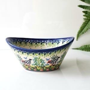 May include: A ceramic bowl with a blue rim and a decorative pattern of birds and flowers. The bowl has a curved shape and is painted with a detailed floral design in blue, green, and red. The bowl is approximately 10 inches wide.