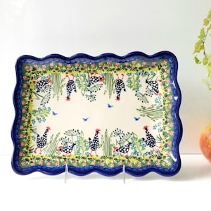 May include: Rectangular ceramic serving platter with a scalloped blue rim. The platter features a white background with a painted design of chickens, plants, and blue birds. The border has a green and blue floral pattern.
