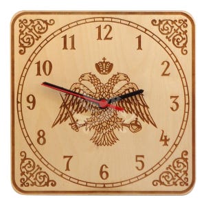 Pode incluir: Um relógio de madeira com fundo castanho claro e marcadores de hora romanos pretos. O mostrador do relógio apresenta uma imagem estilizada de uma águia de duas cabeças com uma coroa e uma espada. Os ponteiros do relógio são pretos e vermelhos.