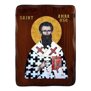 Op de afbeelding: Houten religieuze icoon van Sint Ambrosius, met een gouden halo en de tekst "SAINT AMBROSE". De heilige wordt afgebeeld met een lange zwarte baard, een boek vasthoudend. Het icoon heeft een donkerbruine houten achtergrond.