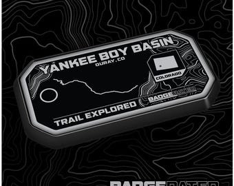 May include: A black and white trail badge with the text "Yankee Boy Basin, Ouray, CO" and "Trail Explored" with a map of the trail and a small Colorado flag. The badge is made by BadgeRated.