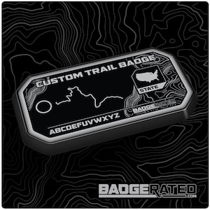 Peut inclure: Un badge de sentier personnalisé noir et argent avec une carte d'un sentier, le texte "CUSTOM TRAIL BADGE", "ABCDEFUVWXYZ", et "STATE" et le logo "BADGERATED".